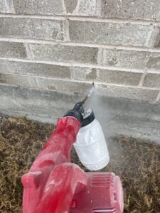 Exclusion service applying protective spray along brick foundation in Melissa.