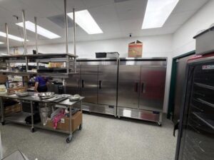 Stainless steel food-prep kitchen with refrigerators and prep tables during a cockroach monitoring inspection in Legacy West, Plano, Texas.