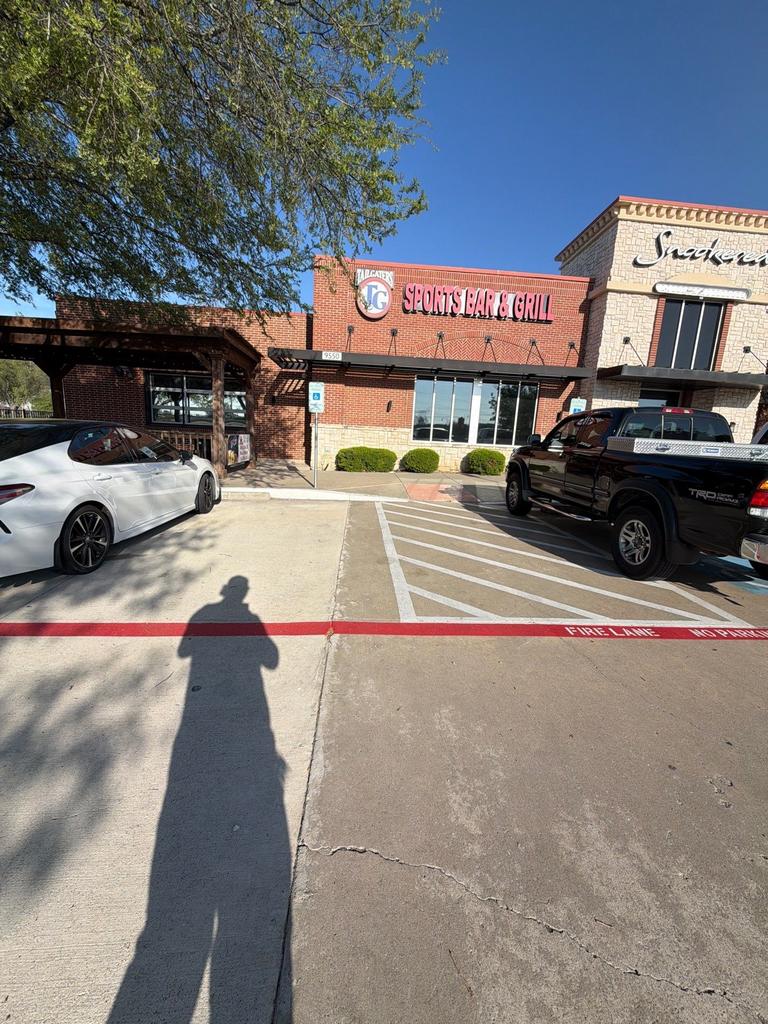Technician conducts an exterior rodent prevention inspection at a commercial sports bar and grill entrance and parking area in Frisco, Texas.