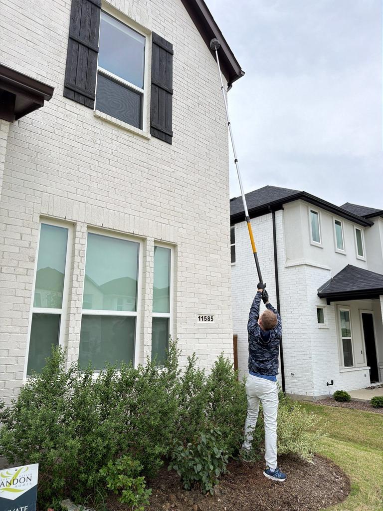 Technician uses an extension duster to remove spider webs from second-story eaves during exterior service at a home in Allen, Texas.