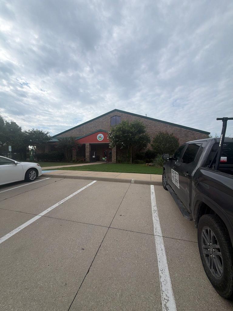 Pest Me Off service truck parked by a commercial building entrance during a general pest control visit in Stonebridge Ranch, McKinney, Texas.
