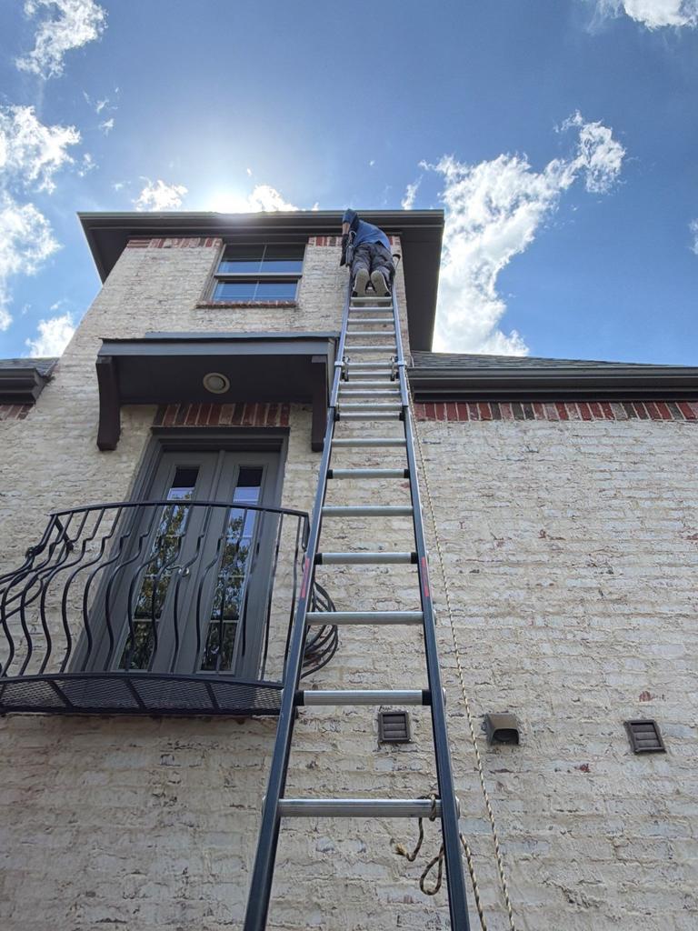 A technician on a tall ladder inspects the second-story soffit for wasp nesting activity at a residential home in McKinney, Texas.