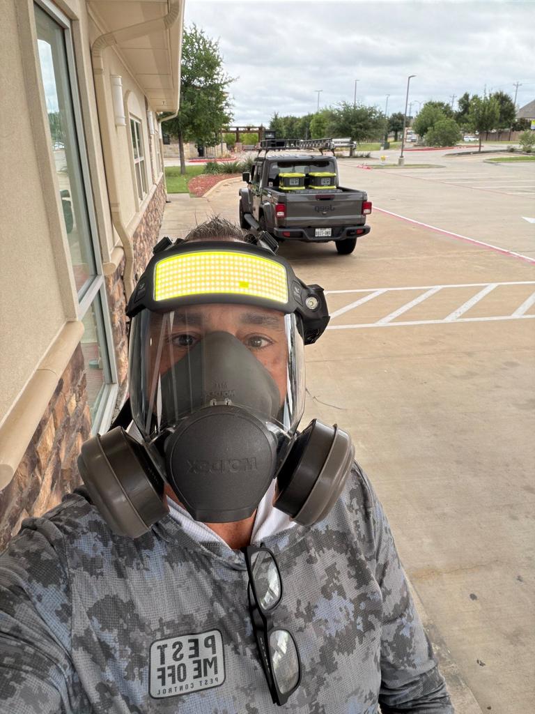 Pest control technician wearing a full-face respirator and protective gear outside a commercial building in Stonebridge Ranch, McKinney, Texas before treatment.