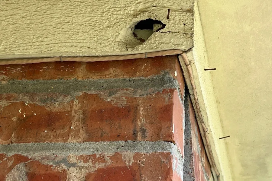 Pest Control Carrollton, TX 13 Open hole in painted wood fascia at a brick corner, a rodent entry point on a Pest Me Off job in Carrollton, TX
