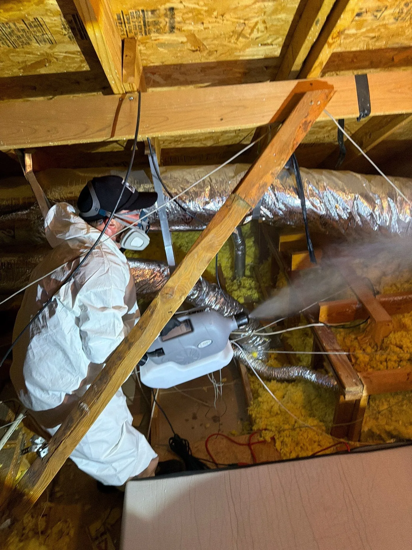 Pest Me Off technician in a protective suit treating a McKinney TX attic after a rodent removal, the sanitation step before sealing