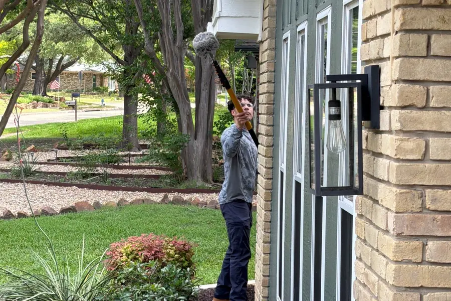 Pest Me Off technician removing spider webs from a roofline in Plano, TX