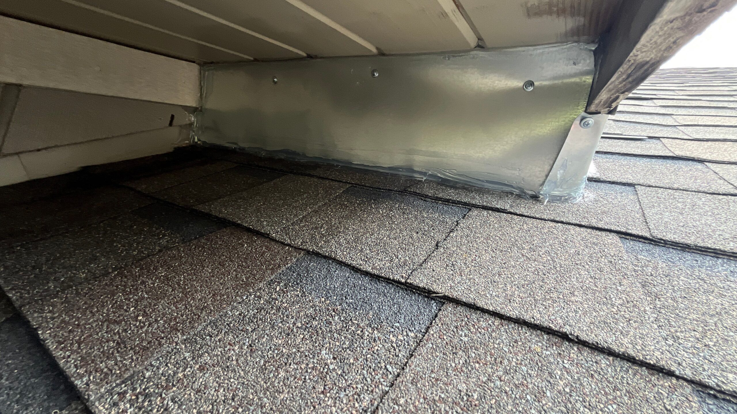 Metal sheet flashing fastened and sealed over a gap where the roofline meets the siding, above asphalt shingles.